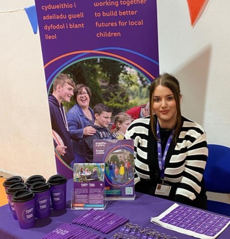 Lady in a black and white striped cardigan sat at a table with branded merchandise for Foster Wales Merthyr Tydfil
