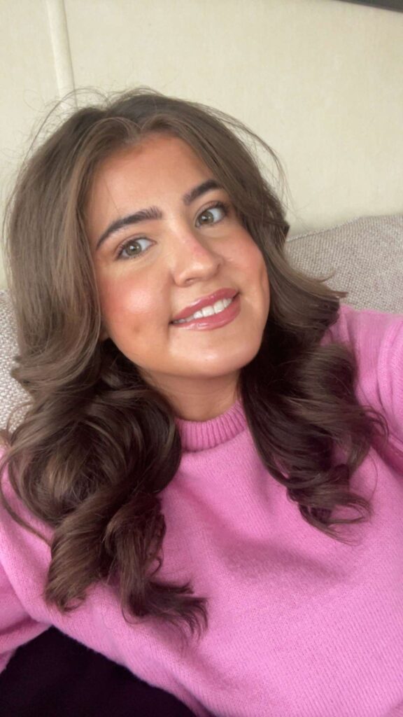 Nell, smiling brunette in a pink jumper
